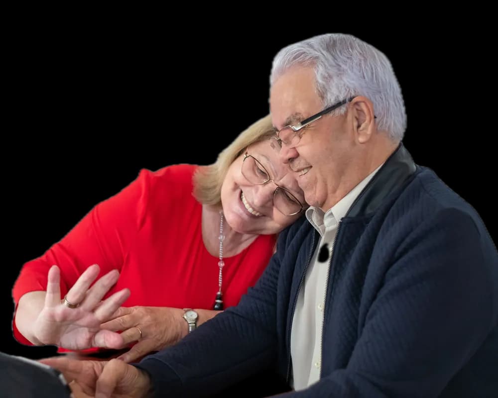 An older couple, heads together, smiling and waving at a tablet