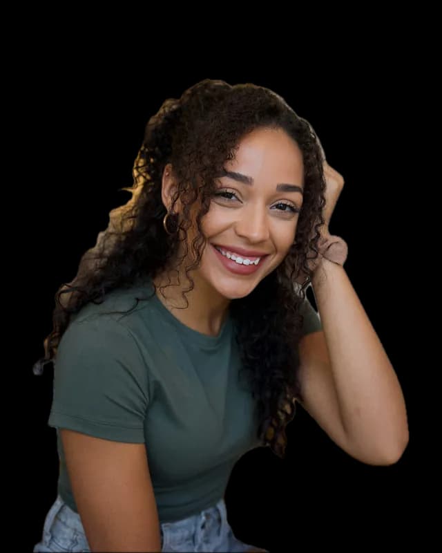 A smiling young woman with long curly hair, one hand resting in it