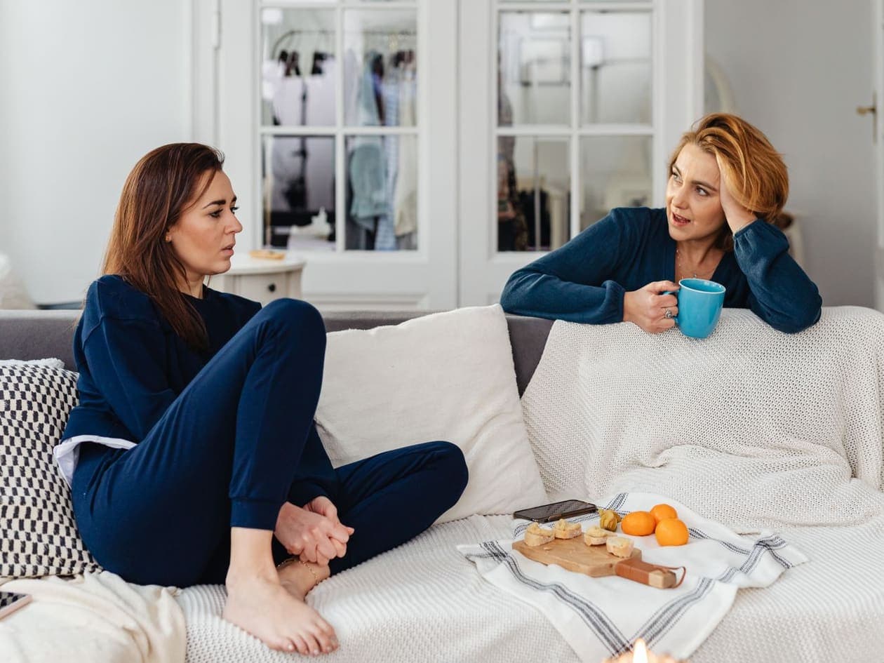 Two women at home on a sofa, one with a cup of tea, talking things over