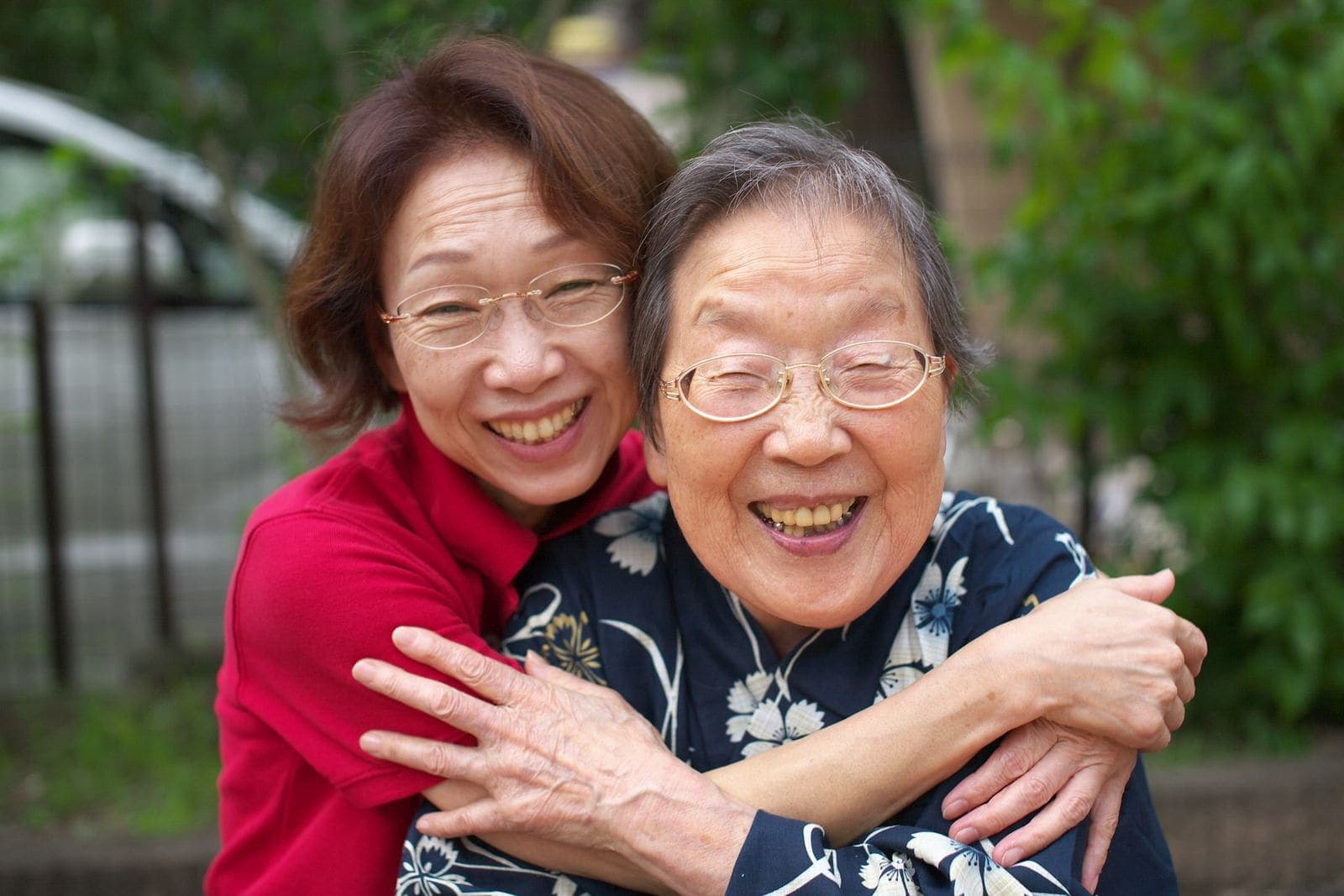 An older mother and her grown daughter hugging and laughing together outdoors