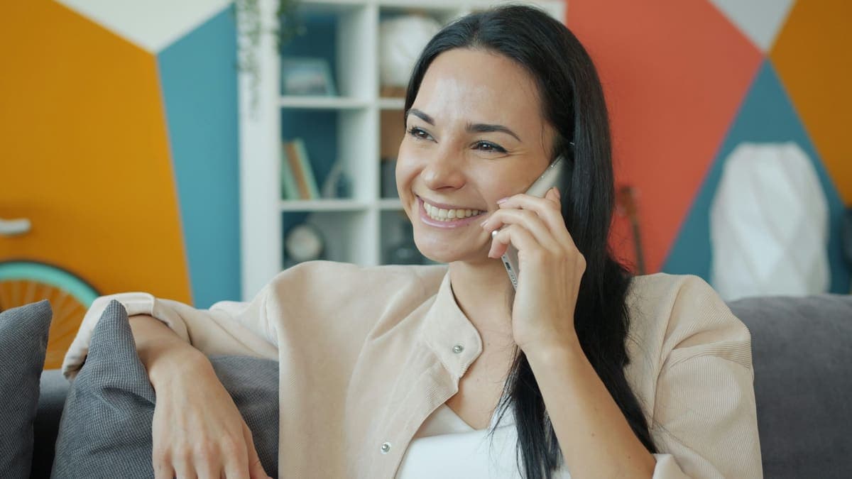 A woman smiling on a phone call, sitting on her sofa at home