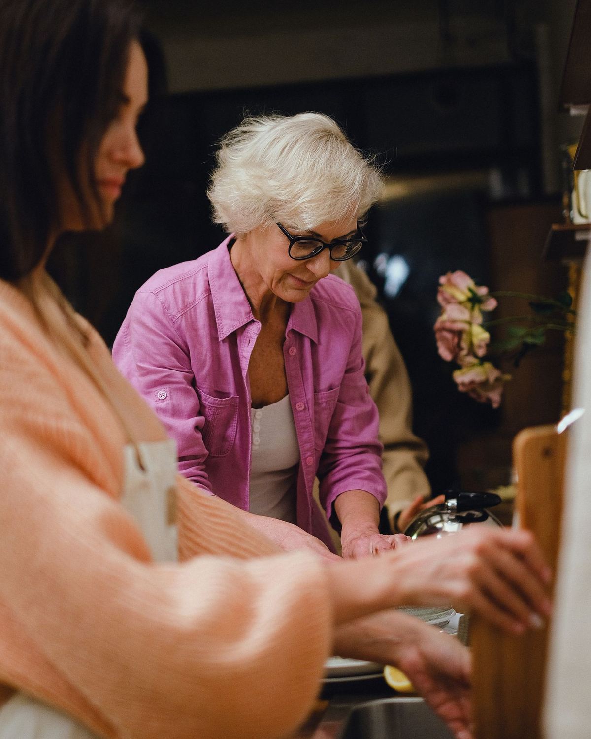 An adult daughter and her mother preparing a meal together in a home kitchen.